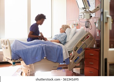 Hospital Nurse With Digital Tablet Talks To Senior Patient