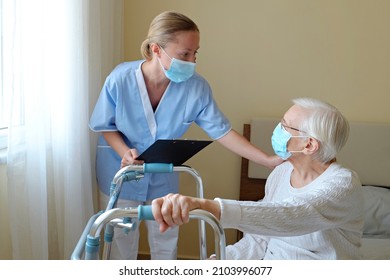 Hospital Nurse Wearing A Face Mask, Holding A Clipboard With Medical History For An Elderly Lady. Senior Woman And Her Designated Care Giver Discussing Test Results. Background, Close Up, Copy Space.