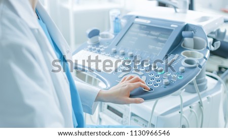 In the Hospital, Obstetrician Pushes Buttons on a Control Panel Before Starting Ultrasound / Sonogram Procedure.