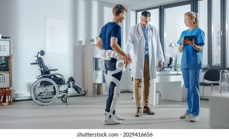 Hospital Physical Therapy: Doctor And Rehabilitation Specialist Use Tablet Computer, Helps Disabled Patient With Injury Walks While Wearing Advanced Robotic Exoskeleton Legs. Advanced Physiotherapy