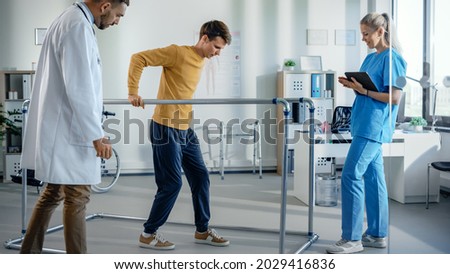 Hospital Physical Therapy Room: Patient with Injury Walking Holding for Parallel Bars, Professional Physiotherapist and Doctor Assist, Help, Train Disabled Person Do Rehabilitative Physiotherapy