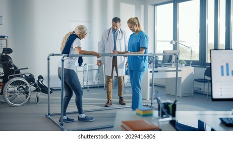 Hospital Physical Therapy: Strong Senior Female Disabled Patient With Injury Making First Steps, Walks Holding For Parallel Bars. Physiotherapist, Rehabilitation Doctor Applaud, Encourage Old Woman