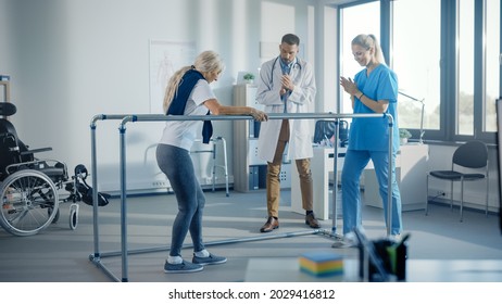 Hospital Physical Therapy: Strong Senior Female Disabled Patient With Injury Making First Steps, Walks Holding For Parallel Bars. Physiotherapist, Rehabilitation Doctor Applaud, Encourage Old Woman