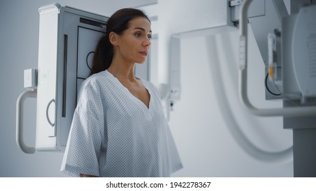 Hospital Radiology Room: Beautiful Multiethnic Woman Standing In Medical Gown In The X-Ray Machine. Adult Female Undergoes Healthcare Exam And Is Scanning Chest, Heart, Lungs In Modern Clinic Office.