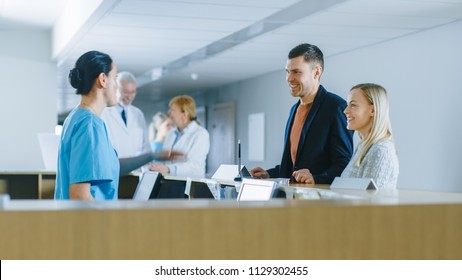 In The Hospital At The Reception Desk Nurse On Duty Answers Young Couple Patients And Showing Them A Way.