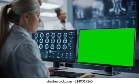 Hospital Research Lab: Female Medical Biotechnology Scientist Working On Green Screen Chroma Key Computer With Brain Scan MRI Images. Background: Neuroscientists Have Meeting Analysing MRI Scan