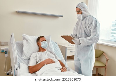 In a hospital room, a healthcare worker in protective gear consults a patient, emphasizing the importance of proper medical care and ensuring their safety during this critical time - Powered by Shutterstock