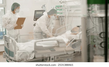 A hospital scene with two healthcare workers in full protective gear monitoring a male patient in an ICU bed, surrounded by medical equipment, highlighting critical care and medical attention. - Powered by Shutterstock