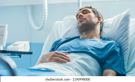 In The Hospital Sick Male Patient Lies On A Bed Sleeping, Heart Rate Monitor On His Finger. Bright And Modern Medical Ward.