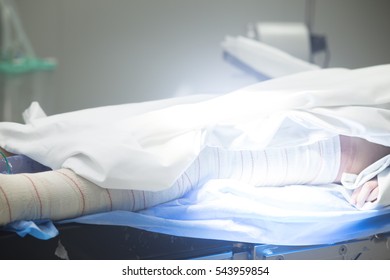 Hospital Surgery Bed And Patient With Leg Bandaged Post Operation In Operating Theater Emergency Room.