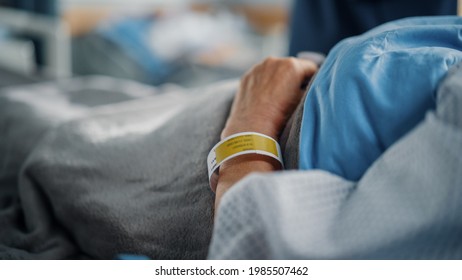 Hospital Ward Bed: Recovering Old Patient Lying in the Hospital Bed Sleeping, Her Fragile Hands Resting on a Blanket, on it Information Wristband. Focus on the Hand.