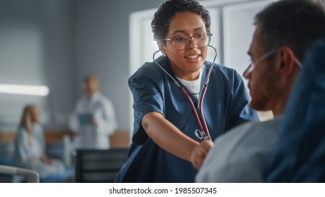 Hospital Ward: Friendly Black Head Nurse Uses Stethoscope To Listen To Heartbeat And Lungs Of Recovering Male Patient Resting In Bed, Does Checkup. Man Getting Well After Successful Surgery