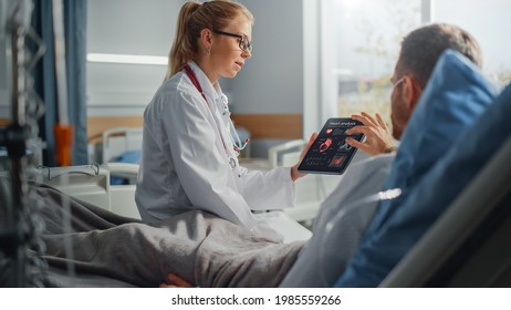 Hospital Ward: Friendly Female Doctor Talks To Sick Male Patient Resting In Bed, Uses Tablet Computer, Shows And Explains Heart Scan Results. Physician Talks To A Man Recovering After Surgery