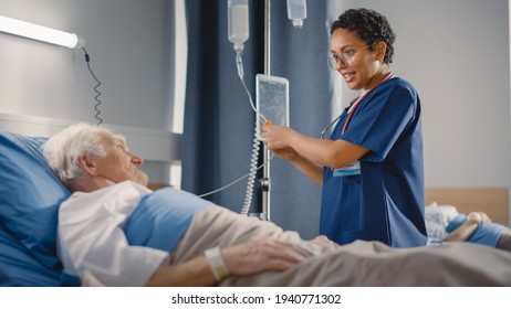 Hospital Ward: Friendly Female Head Nurse Making Rounds Does Checkup On Elderly Patient Resting In Bed. She Checks Computer For Vitals While Old Man Fully Recovering After Successful Surgery