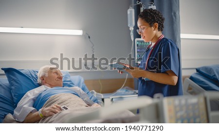 Hospital Ward: Friendly Female Head Nurse Making Rounds does Checkup on Elderly Patient Resting in Bed. She Checks Computer for Vitals while Old Man Fully Recovering after Successful Surgery