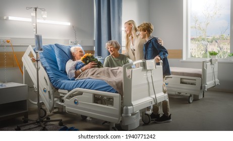 Hospital Ward: Grandfather Resting in Bed, His Caring Beautiful Grandmother Sitting Beside, Happy Grandson and Daughter Visit, Lovingly Give Flowers. Family Support Old Man Recovering - Powered by Shutterstock