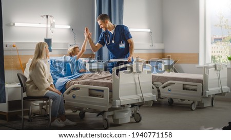 Hospital Ward: Handsome Young Boy Resting in Bed with Caring Mother Visits to Support Him, Friendly Doctor, Surgeon, Nurse Talks, Does High-Five with a Happy Smiling Patient Recovering after Sickness