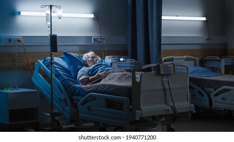 Hospital Ward: Portrait Of Elderly Man Wearing Oxygen Mask Resting In Bed, Struggling To Recover After Covid-19, Sickness, Disease, Surgery. Old Man Fighting For His Life. Dark Blue Sad Shot