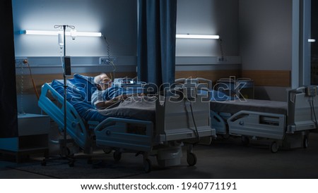 Hospital Ward: Portrait of Elderly Man Wearing Oxygen Mask Resting in Bed, Struggling to Recover after Covid-19, Sickness, Disease, Surgery. Old Man Fighting for His Life. Dark Blue Tragic Shot