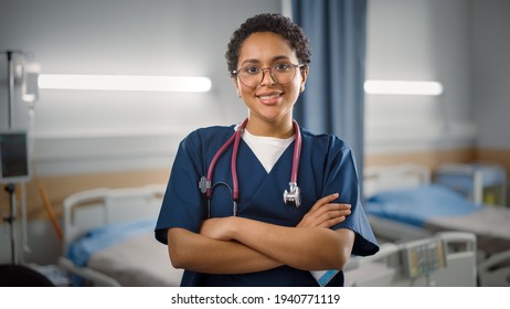 Hospital Ward: Portrait of Posing Beautiful Black Female Head Nurse, Doctor, Surgeon Smiles Charmingly and Kindly Looks at Camera. Modern Clinic with Advanced Equipment and Professional Staff
