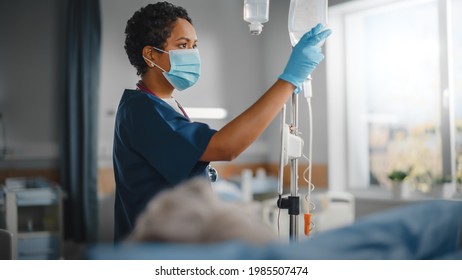Hospital Ward: Professional Black Head Nurse Wearing Face Mask Does Checkup of Patient's Vitals, Checking Heart Rate Computer, Intravenous or Iv Fluids Drip Bag. Caring Nurse Monitors Person Recovery