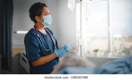 Hospital Ward: Professional Black Head Nurse Wearing Face Mask Does Checkup of Patient's Vitals, Checking Heart Rate Computer, Intravenous or Iv Fluids Drip Bag. Caring Nurse Monitors Person Recovery