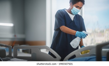 Hospital Ward: Professional Black Nurse Wearing Face Mask, Wiping The Bed, Cleaning Room After Covid-19 Patients Recover. Disinfection, Sterilizing, Sanitizing Clinic After Coronavirus Infected People