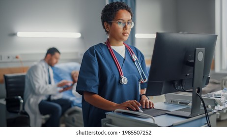 Hospital Ward: Professional Smiling Black Female Head Nurse or Doctor Wearing Stethoscope Uses Medical Computer. In the Background Patients in Beds Recovering Successfully after Sickness and Surgery