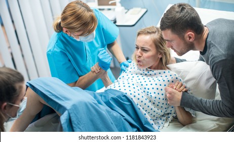 In the Hospital, Woman in Labor Gives Birth, Obstetricians and Doctors Assist, Her Husband Supports Her by Holding Hand. Modern Maternity/ Delivery Ward with Professional Midwives. - Shutterstock ID 1181843923