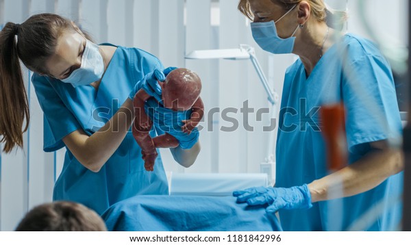 In the Hospital Woman in Labor Pushes
to Give Birth, Baby Comes out, Obstetricians Assist Delivery,
Husband Holds Supports His Wife. Side View
Footage.