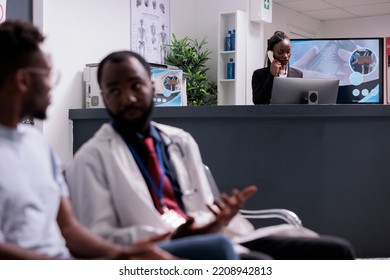 Hospital Worker Using Landline Phone Call To Make Appointments With Specialist At Health Center Facility. Haivng Remote Conversation On Cord Telephone Line With Patients At Reception Counter.