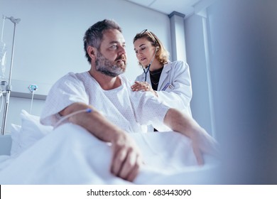 Hospitalised Man Getting Examined By Female Physician. Doctor Checking Heart Beat Of Male Patient In Hospital Room.