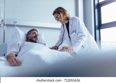 Hospitalized man lying in bed while doctor checking his pulse. Female physician examining male patient in hospital room. - Shutterstock ID 712055626
