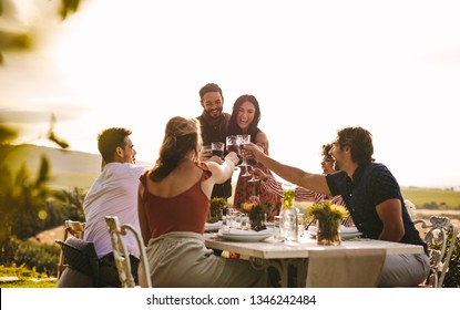 Host Couple Toasting Drinks With Friends At Dinner Party. Cheerful People Celebrating With Drinks At Party.