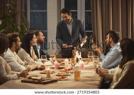 Host pouring wine while friends listening at dinner. Concept of wine tasting culture, lifestyle experiences, friendly rituals, home celebrations and relaxed social communication.