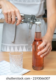 Hostess Girl In A Gray Kitchen Apron Opens A Glass Bottle With A Special Bottle Opener.