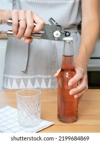 Hostess Girl In A Gray Kitchen Apron Opens A Glass Bottle With A Special Bottle Opener.