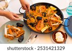 Hostess of house circumcised hands shift sea paella into serving plates, family dinner is served. Womens hands put portions of sea paella with lobster and shrimp on plate