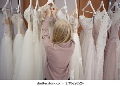 hostess of the wedding salon looks at the wedding dress. Small business, business woman with her own store of wedding and evening dresses, favorite job. A girl looks at a wedding dress for the bride