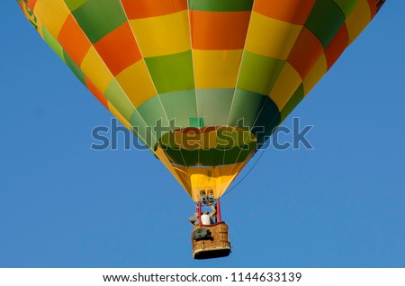 Hot air balloon close cropped showing bottom half of balloon with basket containing three people, Bright colours and blue sky. Air transport and outdoor adventure. Up and away.