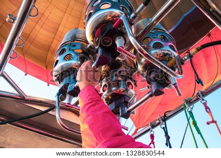 Hot air balloon flight. Close up view inside the dome of aerostat. Hand of pilot or captain holding gas-burner from which the flame escapes.