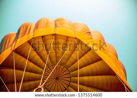 Hot air balloon flying in the blue sky with orange colour fabric parachute open and the ropes hook with the basket