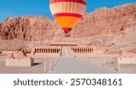 Hot air balloon flying over Hatshepsut Temple at sunrise in Valley of the Kings and red cliffs western bank of Nile river - Luxor- Egypt