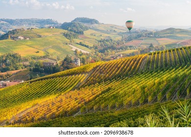 Hot air balloon flying over hills and vineyards during fall season surrounding Barolo village. In the Langhe region, Cuneo, Piedmont, Italy.
