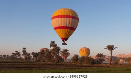 Hot air balloon is inflating before liftoff - Hatshepsut Temple at sunrise in Valley of the Kings and red cliffs western bank of Nile river- Luxor- Egypt - Powered by Shutterstock