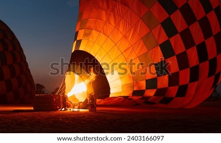 Hot air balloon is inflating before liftoff - Hatshepsut Temple at sunrise in Valley of the Kings and red cliffs western bank of Nile river- Luxor- Egypt