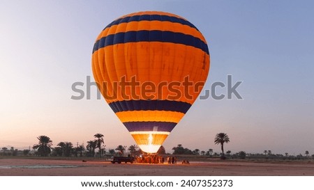 Hot air balloon is inflating before liftoff - Hatshepsut Temple at sunrise in Valley of the Kings and red cliffs western bank of Nile river- Luxor- Egypt