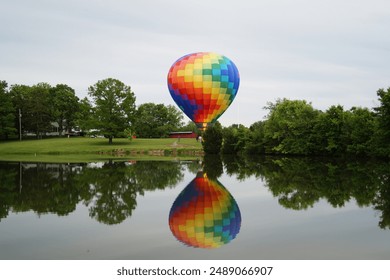 Hot air balloon with reflection hovering above the ground with lake in the foreground