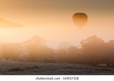 A hot air balloon rises thru the fog just as the sun rises on a cold winter's morning in the Yarra Valley, Victoria, Australia