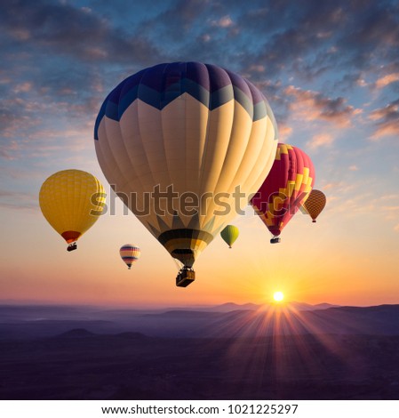 Hot air balloons above ultraviolet mountain silhouettes in golden sunlight. Sunrise in bright colors for your stories about travel dreams, active leisure or adventure.